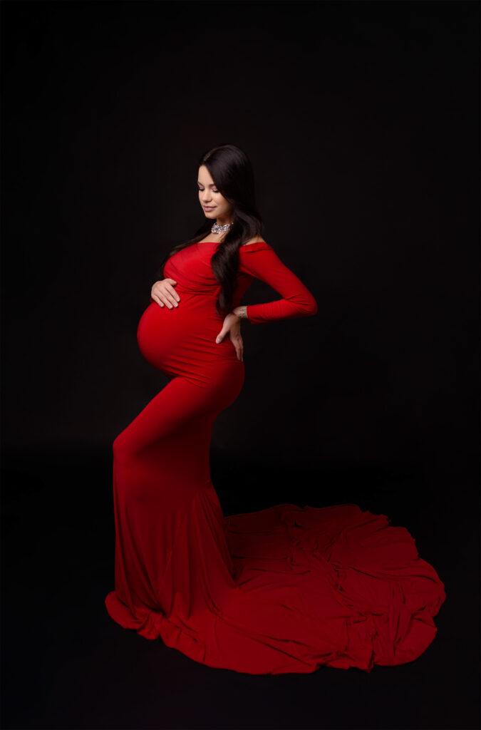 Elegantes Babybauch Shooting im Studio in Kiel – Schwangerschaftsfotografie in rotem Kleid vor schwarzem Hintergrund